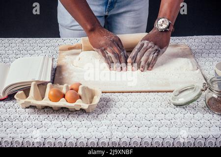 African American male cook chef boasts of pastry hands in flour baking .man`s hands sheets dough with rolling pin bakes cake , the eggs and recipe Stock Photo